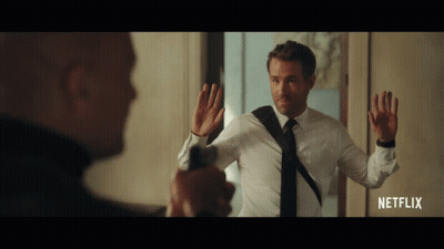 A Man In A White Shirt And Black Tie Is Holding A Gun In Front Of Another Man In A Netflix Advertisement GIF