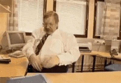 A Man In A White Shirt And Black Tie Is Sitting At A Desk In An Office GIF