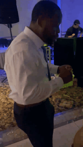 A Man In A White Shirt And Black Tie Is Standing In A Dark Room GIF