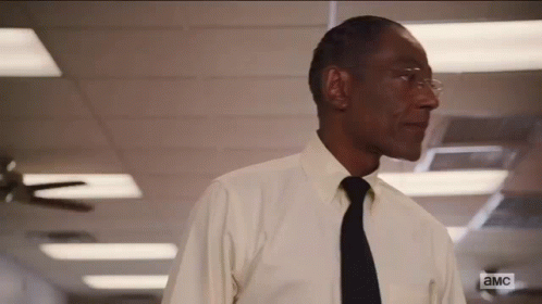 A Man In A White Shirt And Black Tie Is Standing In A Hallway With A Ceiling Fan . GIF