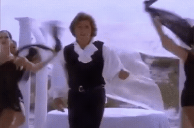 A Man In A White Shirt And Black Vest Is Dancing With Two Women . GIF
