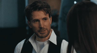 A Man In A White Shirt And Black Vest Looks At A Woman In A Dark Room GIF