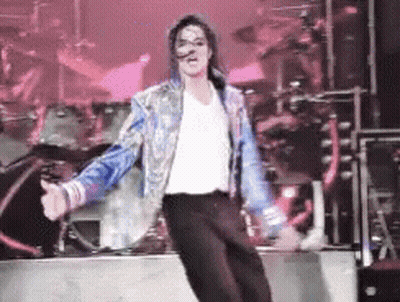 A Man In A White Shirt And Blue Jacket Is Dancing On Stage GIF