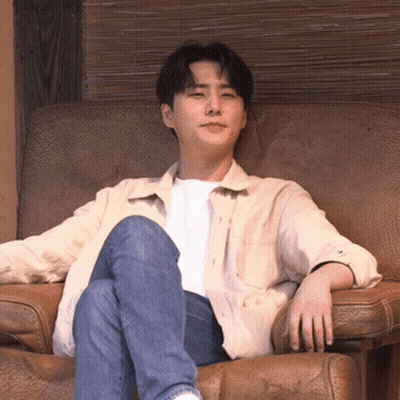 A Man In A White Shirt And Blue Jeans Is Sitting In A Chair GIF