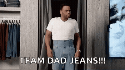 A Man In A White Shirt And Blue Jeans Is Standing In A Dressing Room . GIF