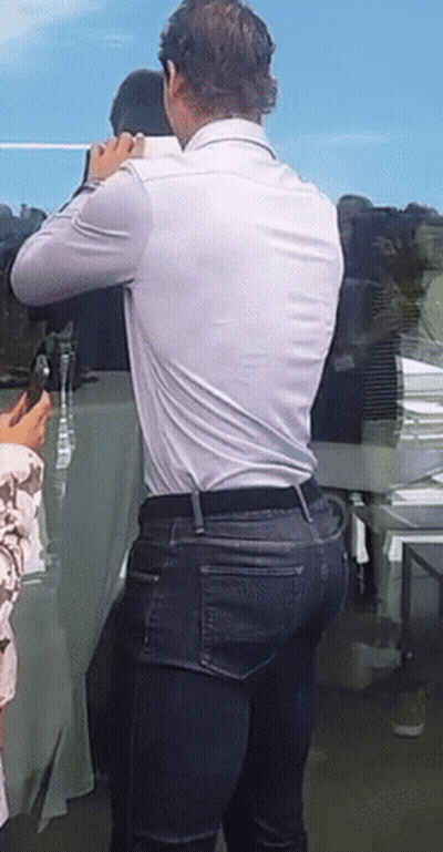 A Man In A White Shirt And Blue Jeans Is Standing In Front Of A Table GIF