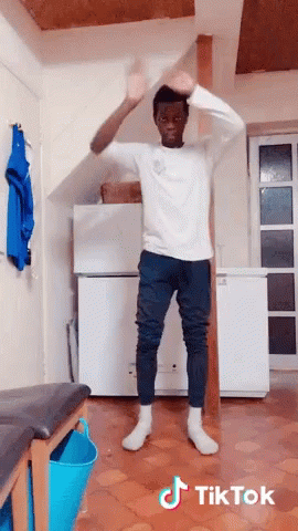 A Man In A White Shirt And Blue Pants Is Dancing In A Room With Tiktok Written On The Bottom Of The Image GIF