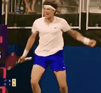 A Man In A White Shirt And Blue Shorts Is Holding A Tennis Racquet In His Hand . GIF