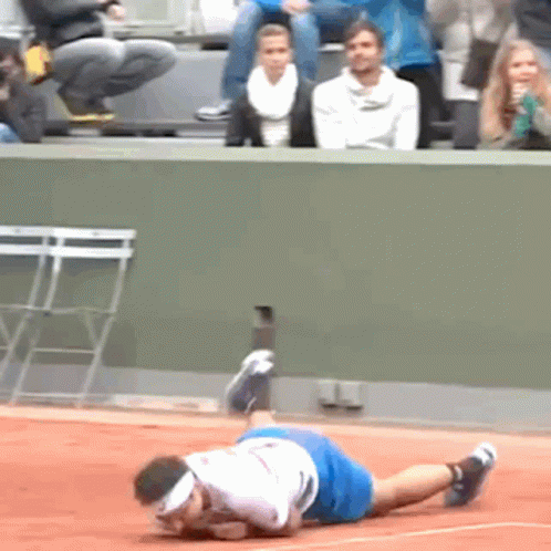 A Man In A White Shirt And Blue Shorts Is Laying On A Tennis Court GIF