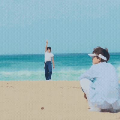 A Man In A White Shirt And Blue Shorts Stands On The Beach GIF