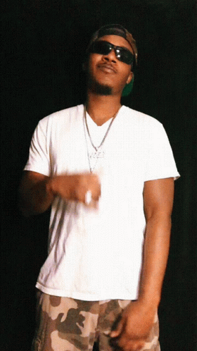 A Man In A White Shirt And Camo Shorts Is Wearing Sunglasses And A Necklace GIF