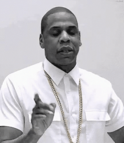 A Man In A White Shirt And Gold Chain Is Pointing At The Camera . GIF