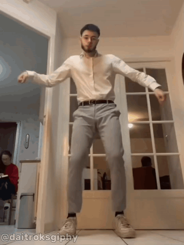 A Man In A White Shirt And Grey Pants Is Dancing In A Hallway With The Hashtag @Daitruksgiphy GIF