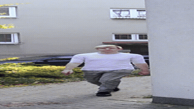 A Man In A White Shirt And Grey Pants Walks Down A Sidewalk GIF