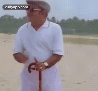 A Man In A White Shirt And Hat Is Holding A Cane . GIF