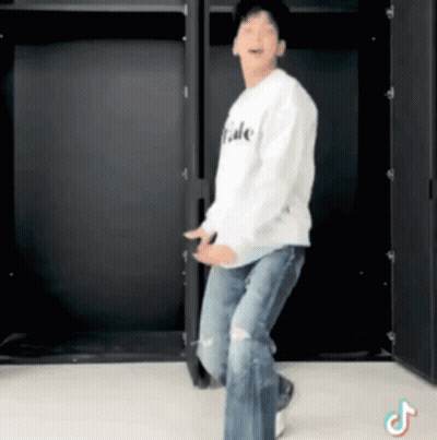 A Man In A White Shirt And Jeans Is Dancing In Front Of A Black Wall . GIF