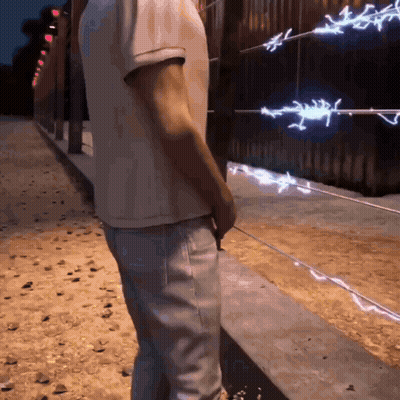 A Man In A White Shirt And Jeans Stands In Front Of A Barbed Wire Fence GIF