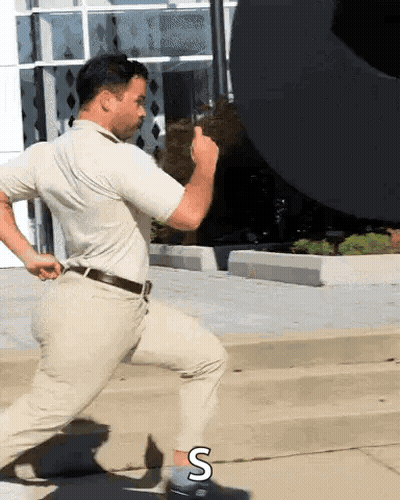 A Man In A White Shirt And Khaki Pants Is Running Down The Street GIF