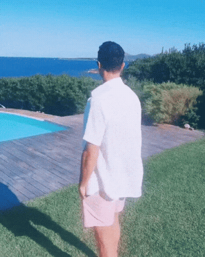 A Man In A White Shirt And Pink Shorts Is Standing In Front Of A Swimming Pool GIF