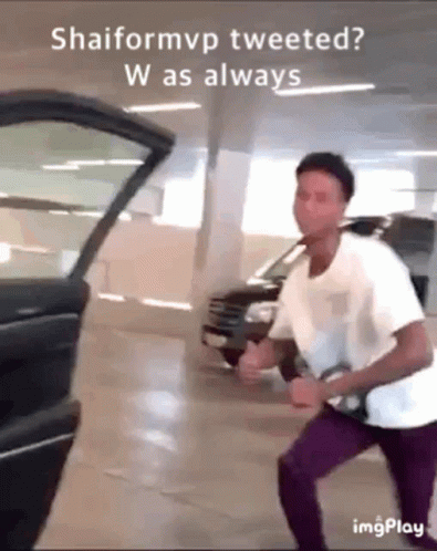 A Man In A White Shirt And Purple Pants Is Standing In Front Of A Black Car . GIF