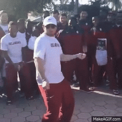 A Man In A White Shirt And Red Pants Is Dancing In Front Of A Crowd Of People . GIF