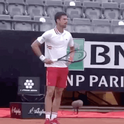 A Man In A White Shirt And Red Shorts Is Holding A Tennis Racket . GIF
