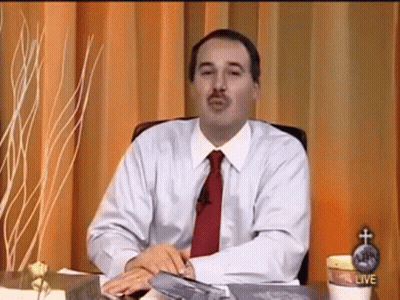 A Man In A White Shirt And Red Tie Is Sitting At A Desk In Front Of A Curtain . GIF