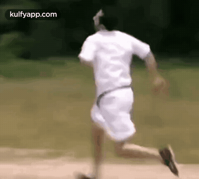 A Man In A White Shirt And Shorts Is Running On A Dirt Road . GIF