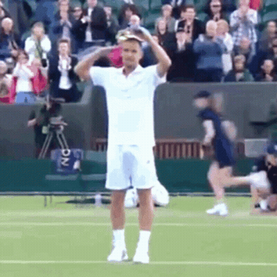 A Man In A White Shirt And Shorts Is Standing On A Tennis Court Holding His Head . GIF