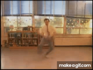 A Man In A White Shirt And Tie Is Dancing In Front Of A Window In A Library . GIF