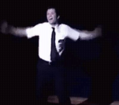 A Man In A White Shirt And Tie Is Dancing On A Stage In The Dark . GIF
