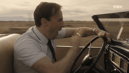 A Man In A White Shirt And Tie Is Driving A Car With The Word Max On The Bottom GIF