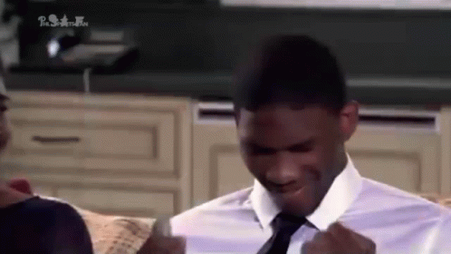 A Man In A White Shirt And Tie Is Sitting On A Couch And Smiling . GIF