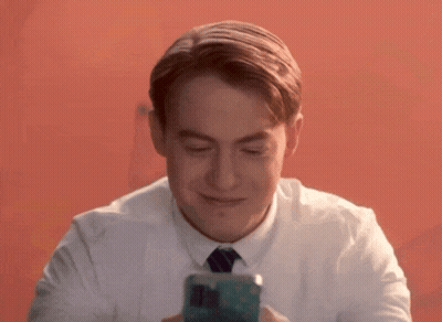 A Man In A White Shirt And Tie Is Smiling And Looking At His Phone GIF