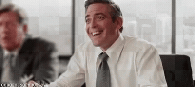 A Man In A White Shirt And Tie Is Smiling While Sitting At A Table In An Office . GIF