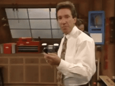 A Man In A White Shirt And Tie Is Standing In A Room Holding A Cell Phone In His Hand . GIF