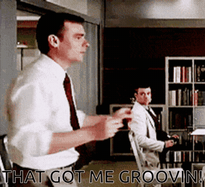 A Man In A White Shirt And Tie Is Standing In Front Of A Bookshelf And Says That Got Me Groovin ! GIF