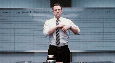 A Man In A White Shirt And Tie Is Standing In Front Of A White Board That Says Sales Revenues GIF