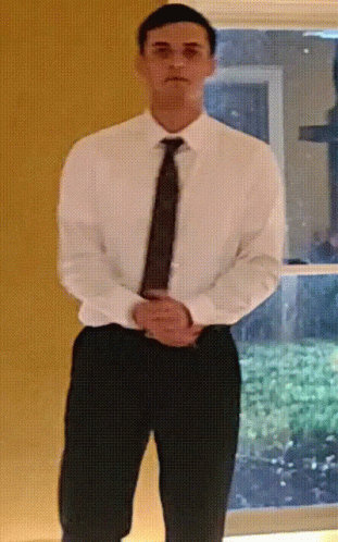 A Man In A White Shirt And Tie Is Standing With His Hands On His Hips GIF