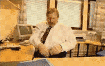 A Man In A White Shirt And Tie Sits At A Desk In Front Of A Computer Monitor GIF