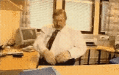 A Man In A White Shirt And Tie Sits At A Desk GIF