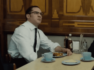 A Man In A White Shirt And Tie Sits At A Table With Plates Of Food GIF