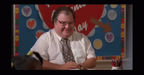 A Man In A White Shirt And Tie Sits In Front Of A Bulletin Board That Says I Love You GIF