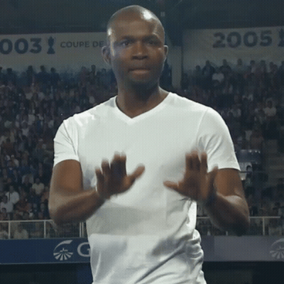 A Man In A White Shirt Applauds In Front Of A Sign That Says 003 GIF