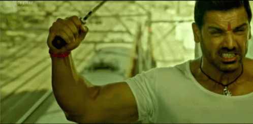 A Man In A White Shirt Holds A Knife In His Hand GIF