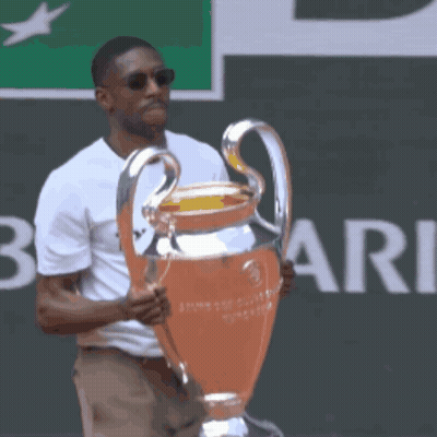 A Man In A White Shirt Holds A Trophy In Front Of A Sign That Says Rie GIF