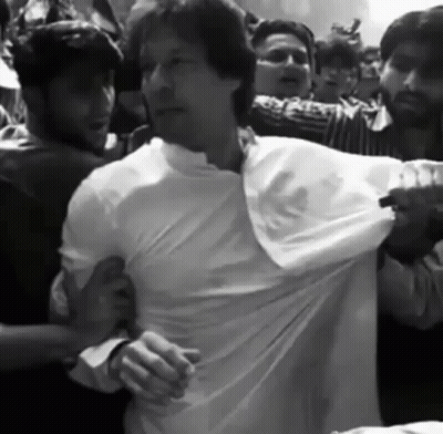 A Man In A White Shirt Is Being Pulled By A Crowd Of People GIF