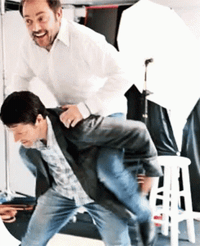 A Man In A White Shirt Is Carrying Another Man On His Shoulders GIF