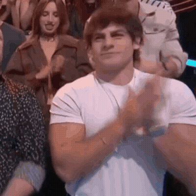 A Man In A White Shirt Is Clapping His Hands In Front Of A Crowd Of People . GIF
