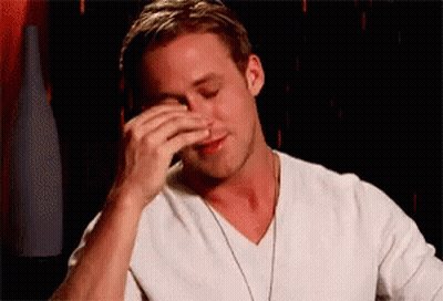 A Man In A White Shirt Is Covering His Face With His Hands . GIF
